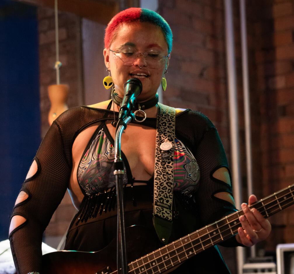 A picture of robi, wearing a patterned shirt and dark pants, testing out a teal guitar.