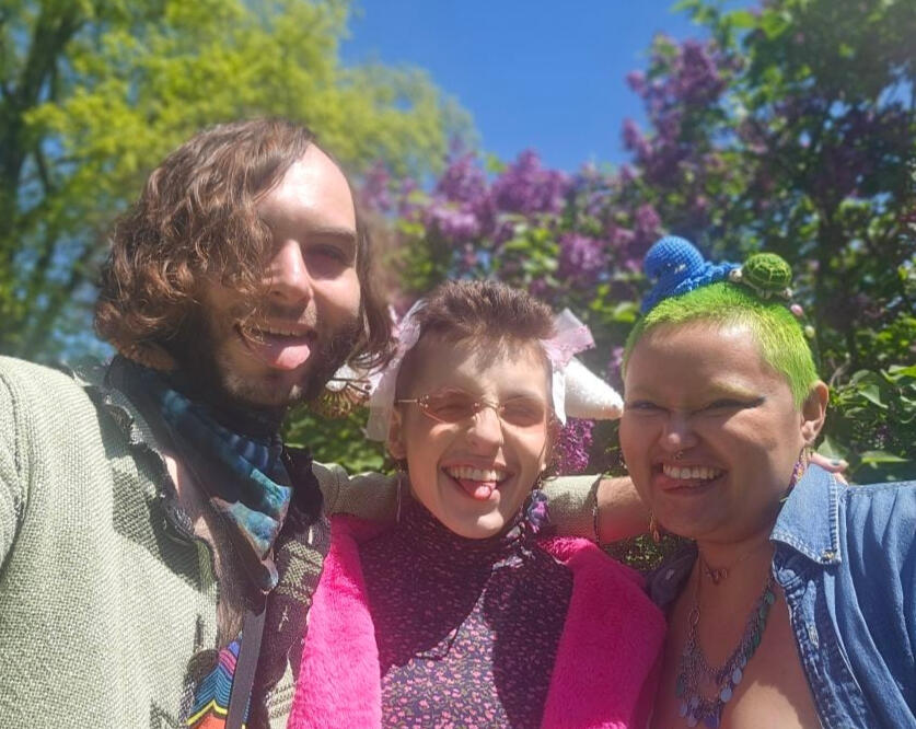 robi's beautiful besties, bandmates, and partners a picture of robi with their two partners smiling and sticking their tongues out in a very brightly lit outdoor area